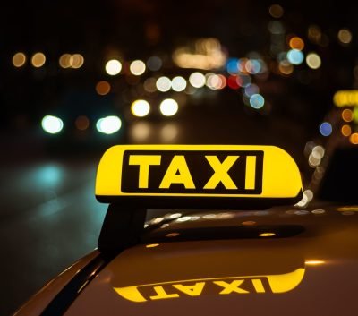 A yellow and black sign of Taxi placed on top of a car at night